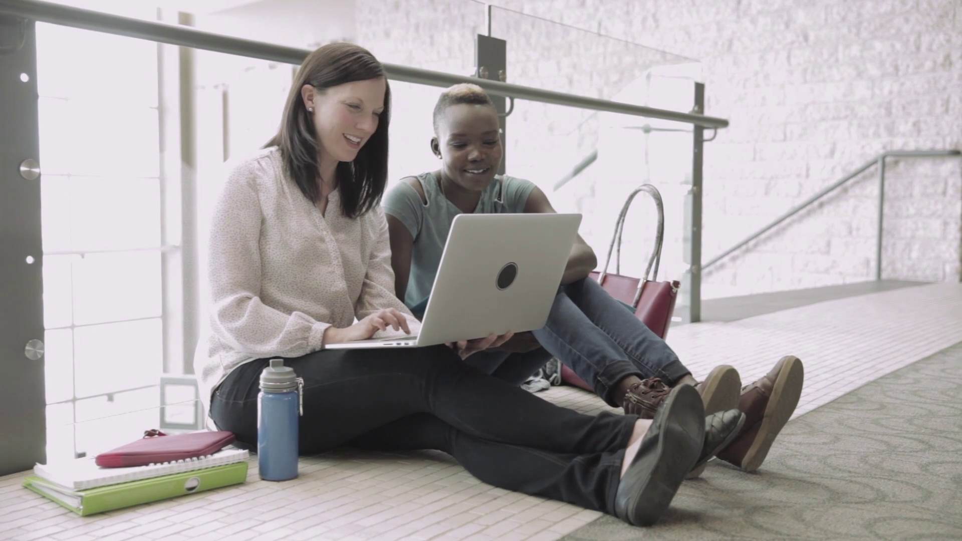 An Educator and Student sit on the floor, looking at a laptop together